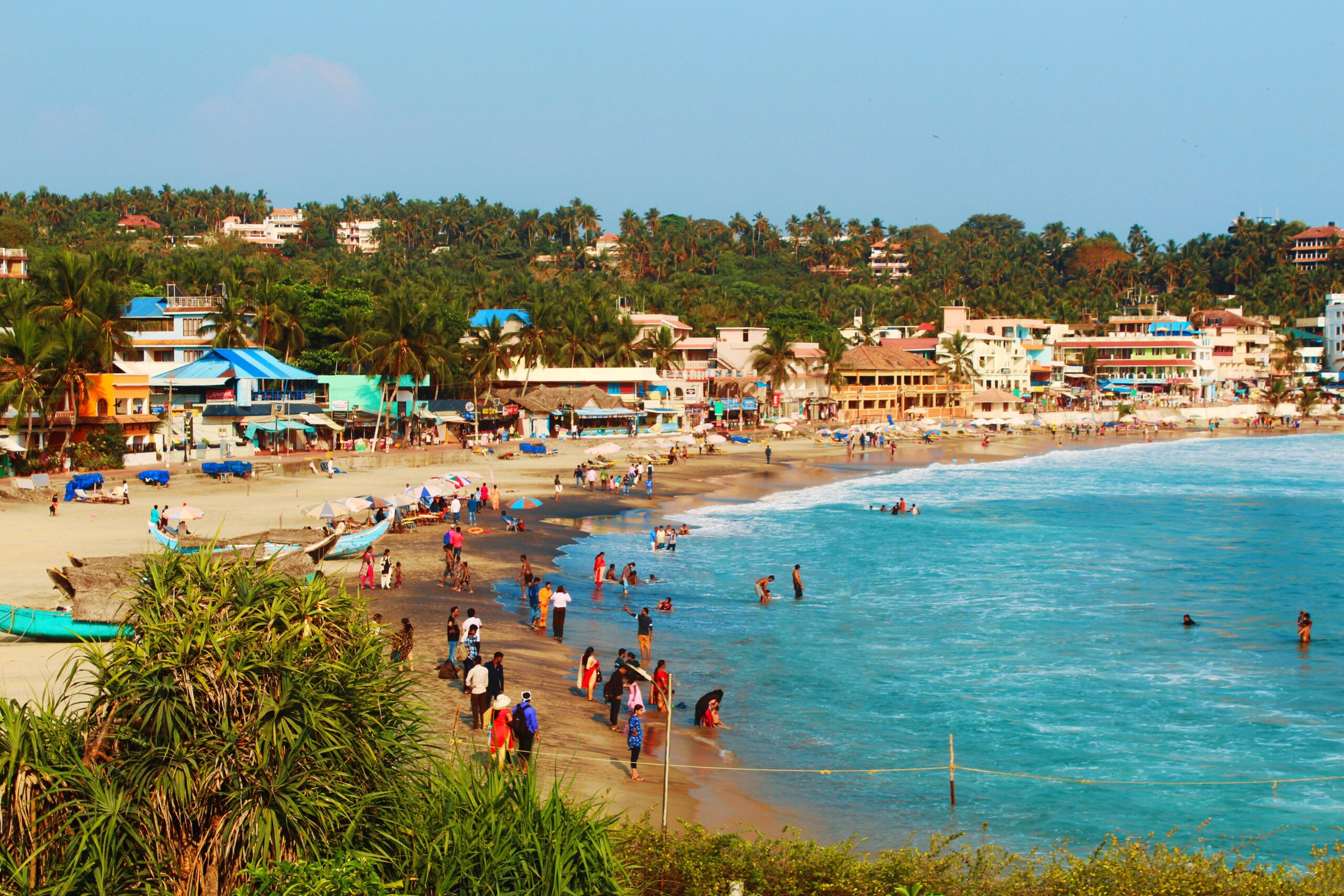 Beachfront village bustling with tourists, vibrant buildings, and palm trees on a sunny day.